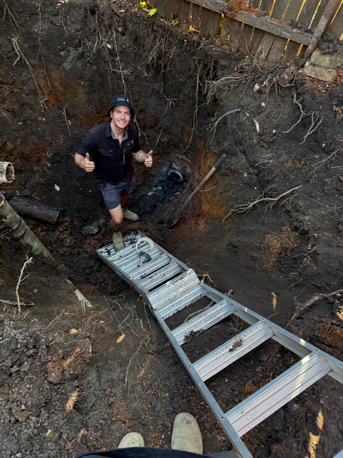 Deep excavation exposing a root-damaged sewer line for replacement
